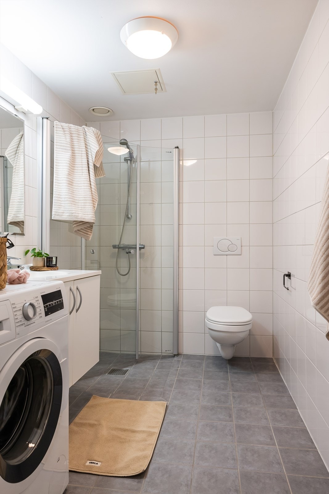 Videre har badet dusj i hjørnet med innfellbare dører og nedsenket gulv samt veggehengt toalett med innebygget sisterne. Det er opplegg for vaskemaskin. Galleribilde