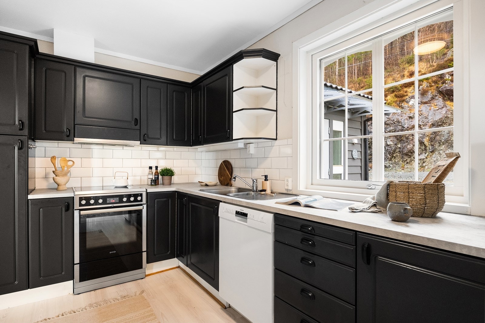 Kjøkkenet er innredet med svartmalt kjøkkeninnredning med profilerte fronter, benkeplate av laminat, stålvask med skyllekum og avrenningsbrett. Galleribilde