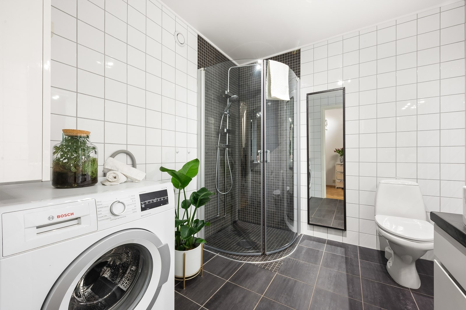 Badet er innredet med gulvstående toalett, dusjhjørne med svingbare glassdører (nyere armatur i dusjen) og baderomsinnredning med skuffer, servant og speil med belysning. Galleribilde