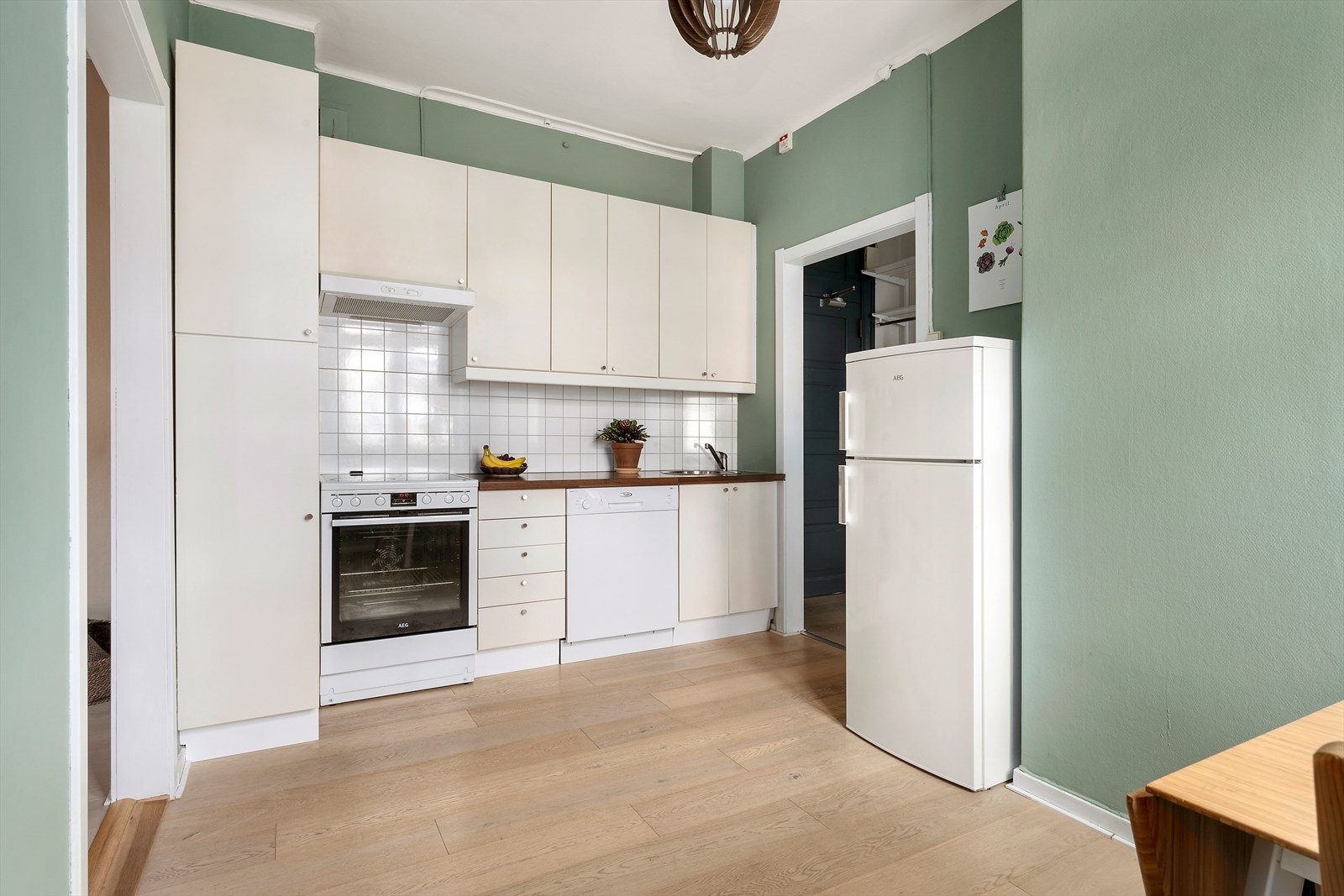 Kjøkkeninnredning med hvite fronter, benkeplater i laminat, ventilator med kullfilter og opplegg for oppvaskmaskin. Fliser over benkeskap Galleribilde