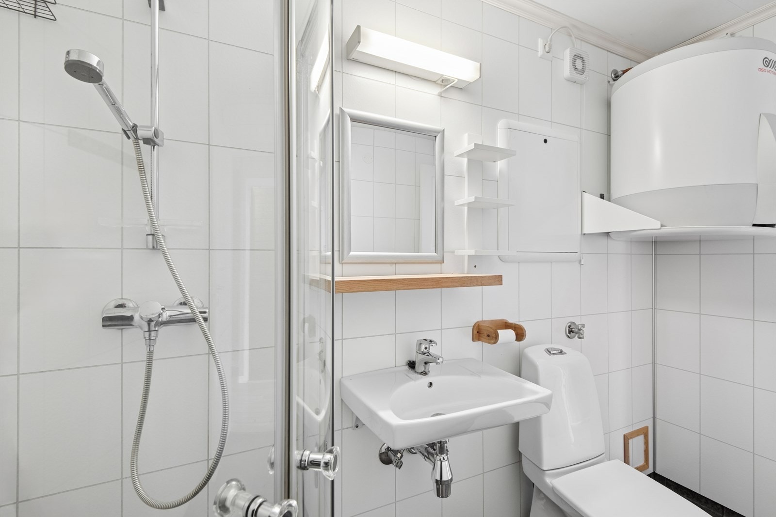 Badet er innredet med et dusjhjørne, toalett, enkel servant og speil med overliggende lys. Det er i tillegg opplegg til vaskemaskin på badet. Galleribilde