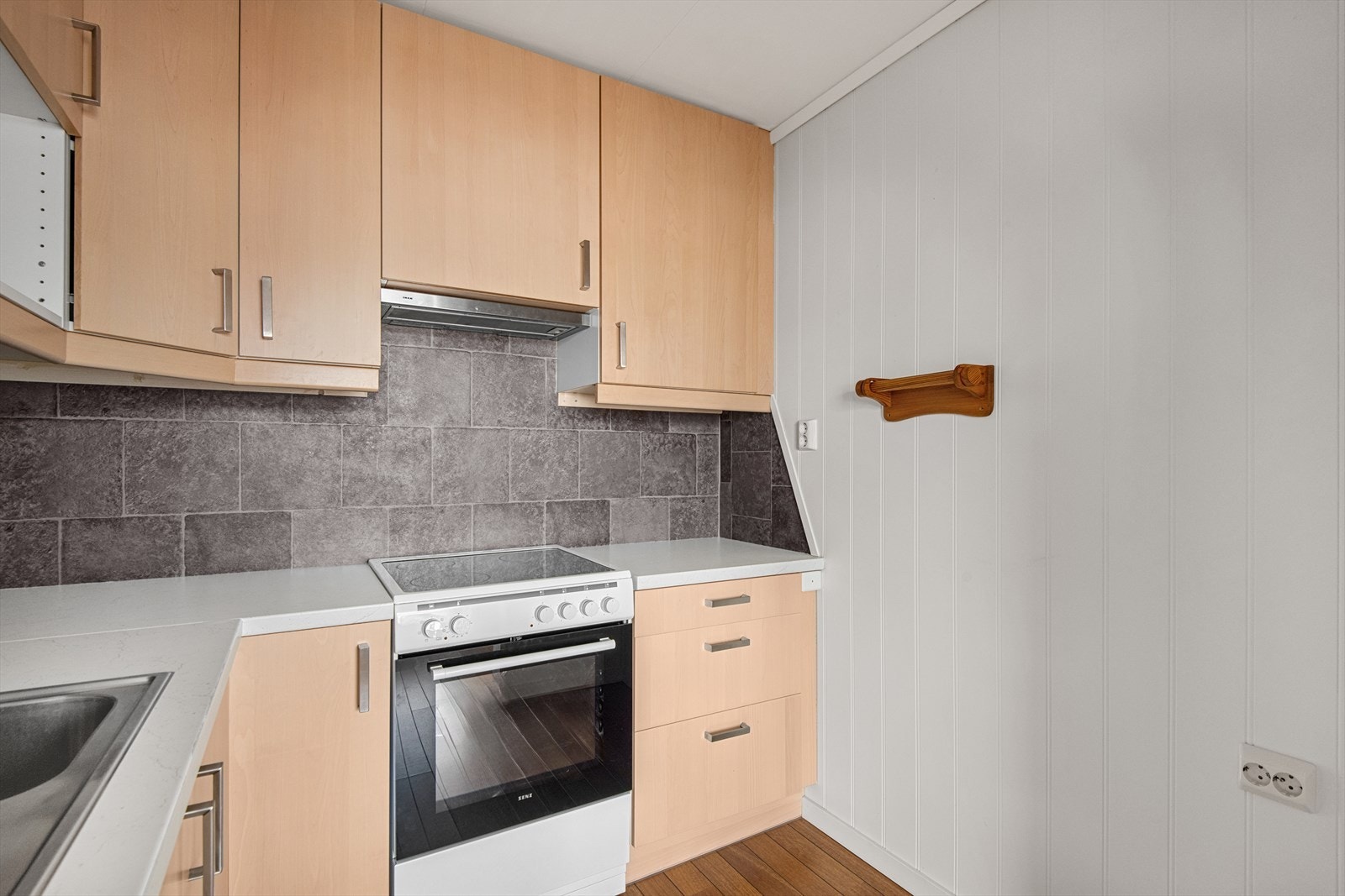 Kjøkkeninnredningen har glatte fronter, laminat benkeplate, nedfelt oppvaskkum, flislignende plater over deler av benk, ventilator og plass til hvitevarer. Galleribilde