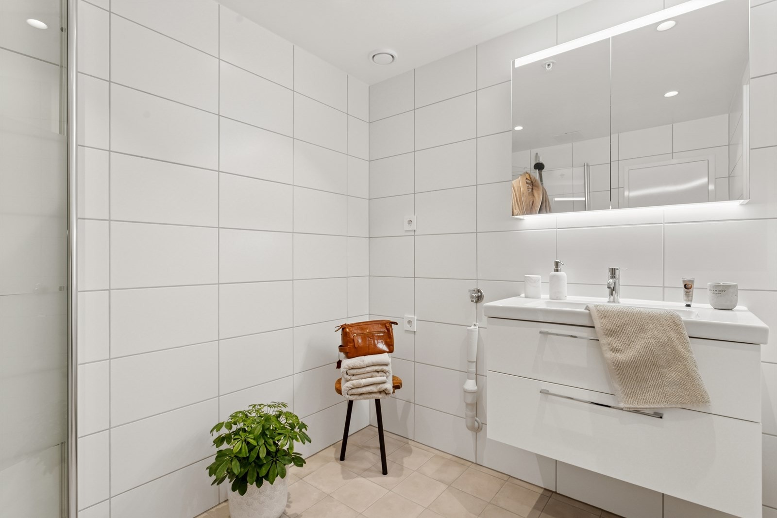 Badet er utstyrt med innfellbare dusjdører, vegghent toalett, servant med underskuffer, speilskap og opplegg til vaskemaskin. Galleribilde