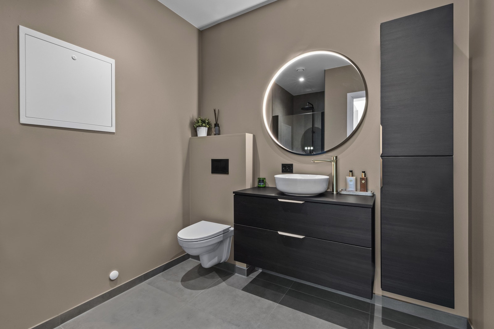 Baderom i 1. etasje med flislagt gulv og slette, malte veggflater. Videre er det vegghengt toalett, servant med innredning og dusjsone med regndusj. Rommet varmes opp med varmekabler. Galleribilde