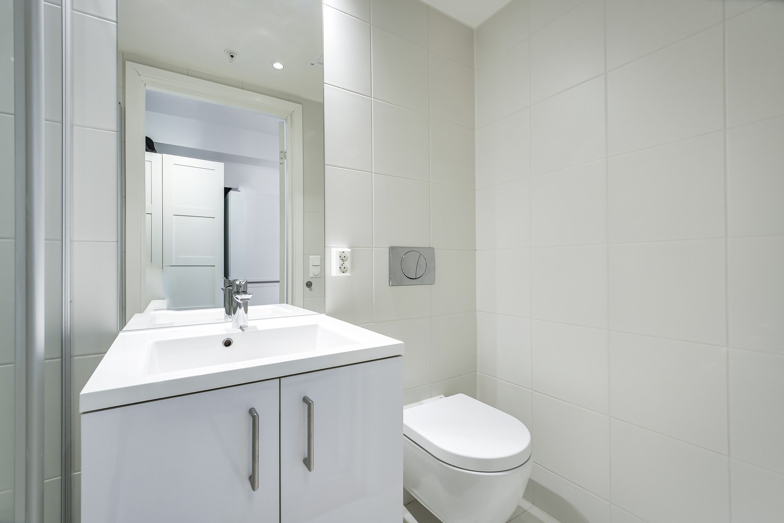 Delikat bad med lyse fliser, vegghengt toalett og moderne servantløsning. Galleribilde