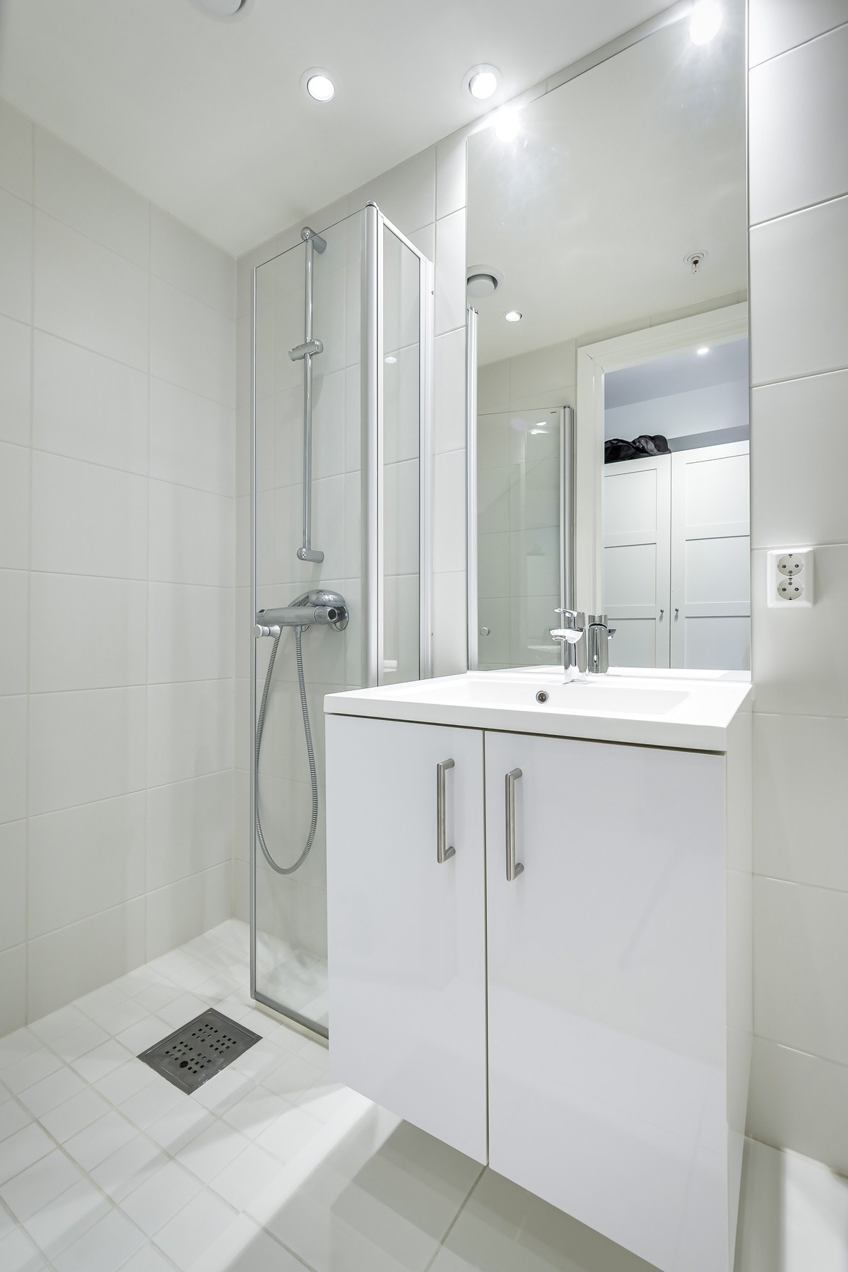 Lyst og funksjonelt bad med servantinnredning, speil og toalett. Praktisk dusjløsning med dusjhjørne og veggmontert armatur. Galleribilde