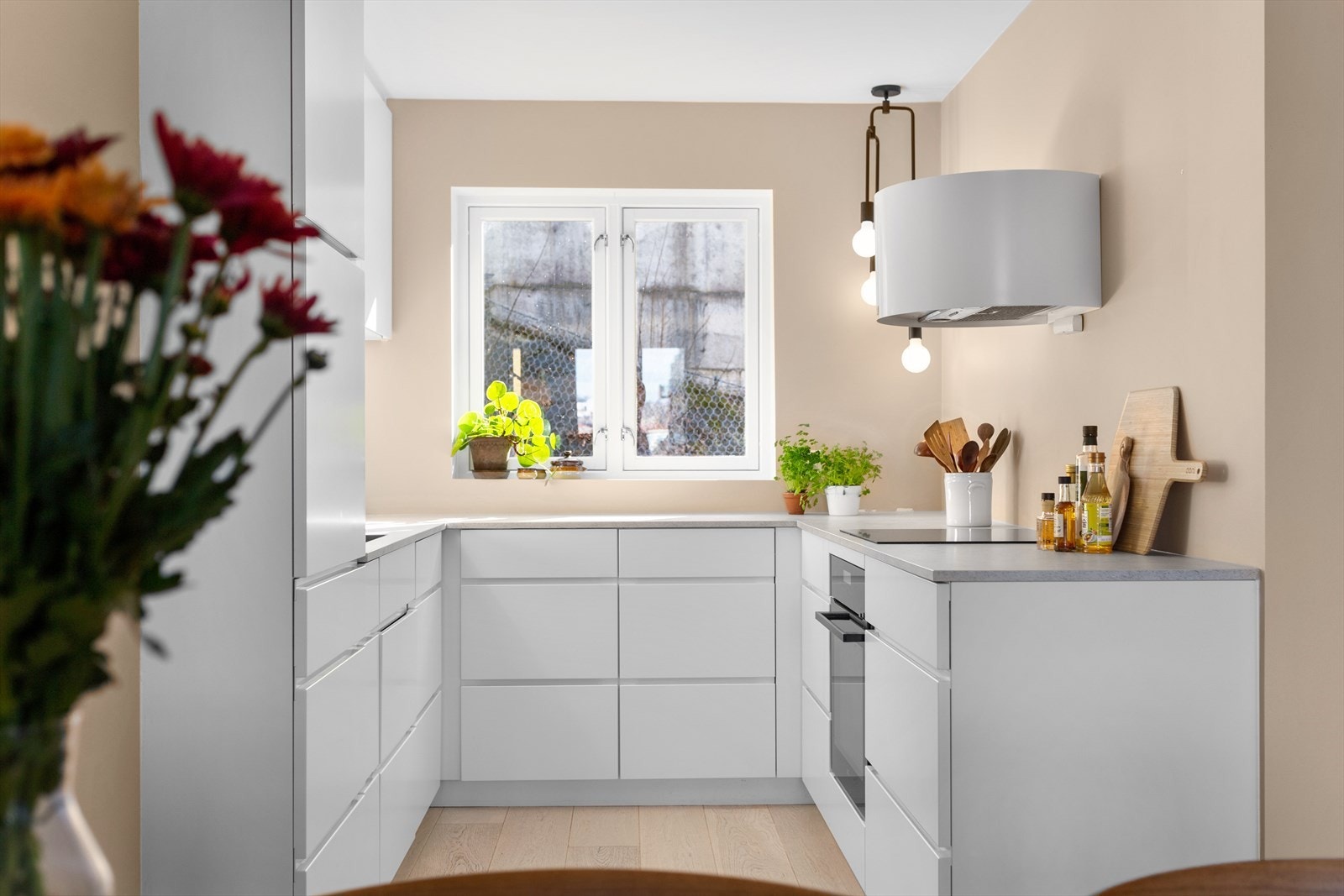 Stilrent kjøkken fra Kvik (2019) med sol gjennom det meste av dagen. Frodig vegetasjon skaper vokser opp og danner en grønn vegg i skråningen foran. Galleribilde