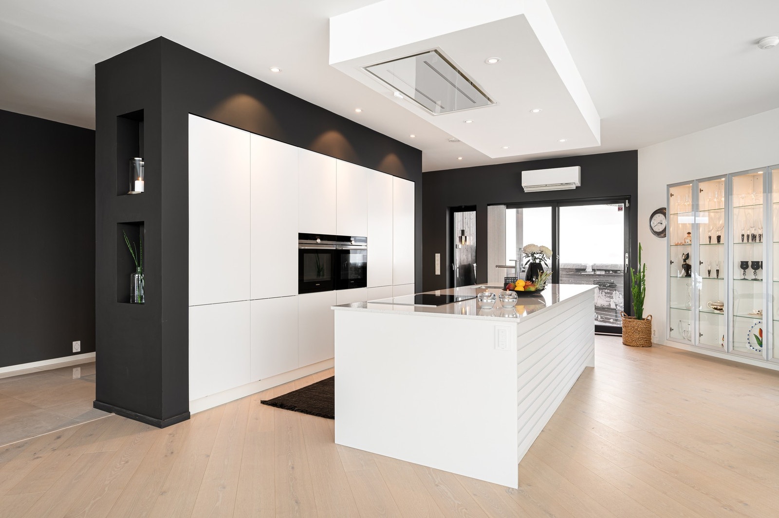 Stilren innredning fra JKE med slette fronter og pen øy med benkeplate i komposittmateriale. Til venstre er det åpent ut mot entre og soveromsavdeling Galleribilde