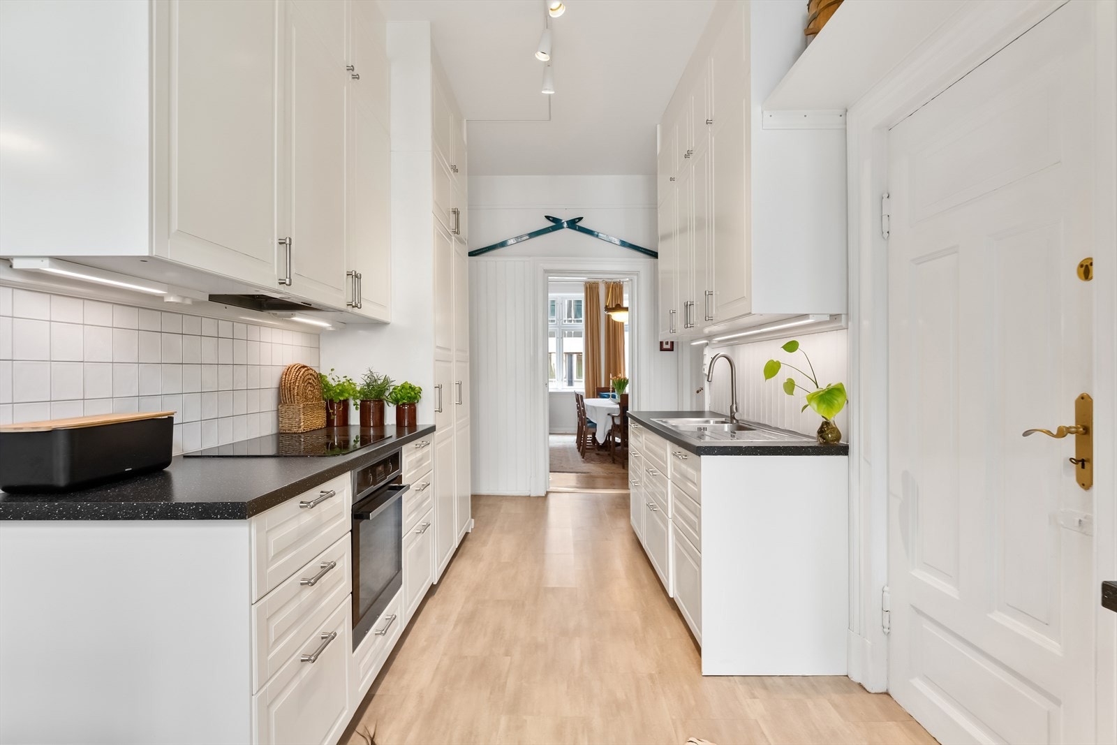 Pen kjøkkeninnredning fra 2015 med profilerte fronter, fliser på vegg over benkeskap og belysning under overskap Galleribilde