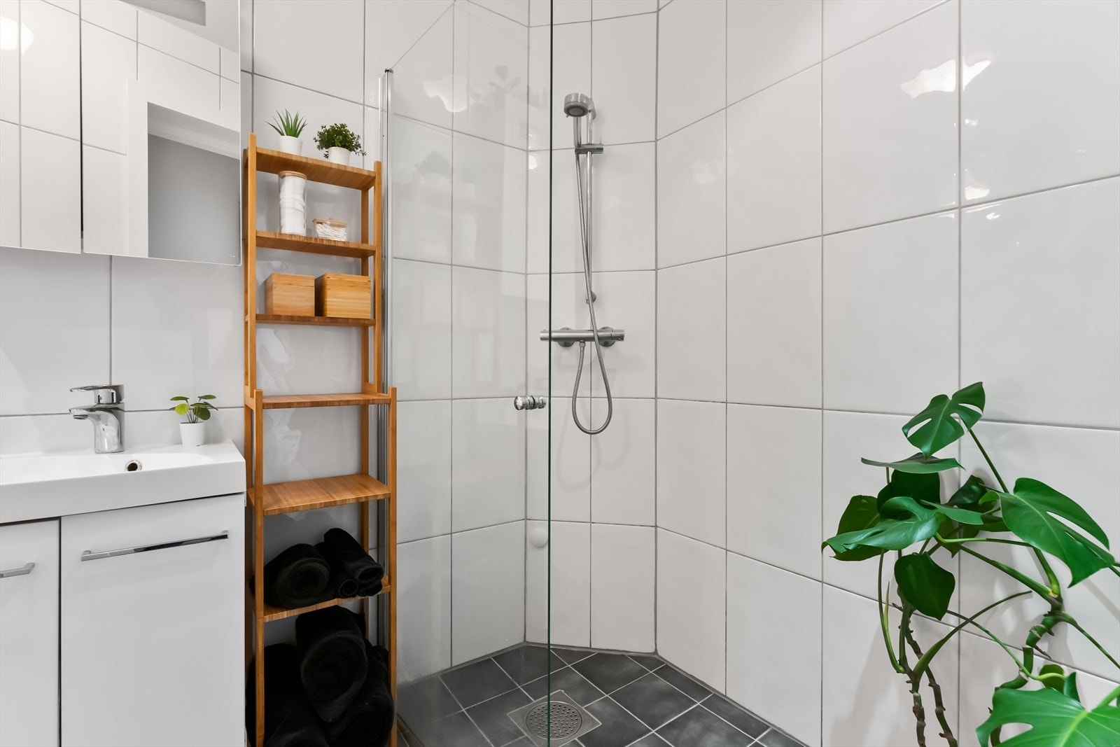 Baderommet er utstyrt med dusj på gulv med dør i glass, veggfestet klosett, servant med innredning og speilfronter- og belysning Galleribilde