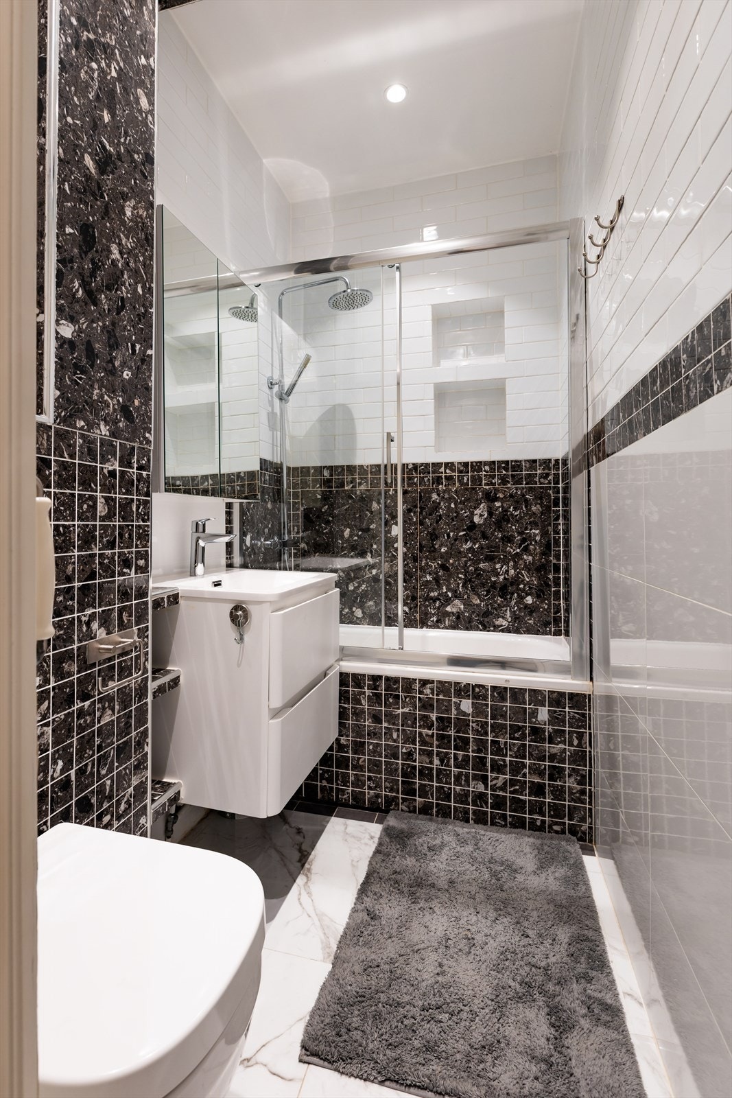 Badet er utstyrt med badekar og regnfallsdusj, samt flislagt hylle i dusjsonen. Galleribilde