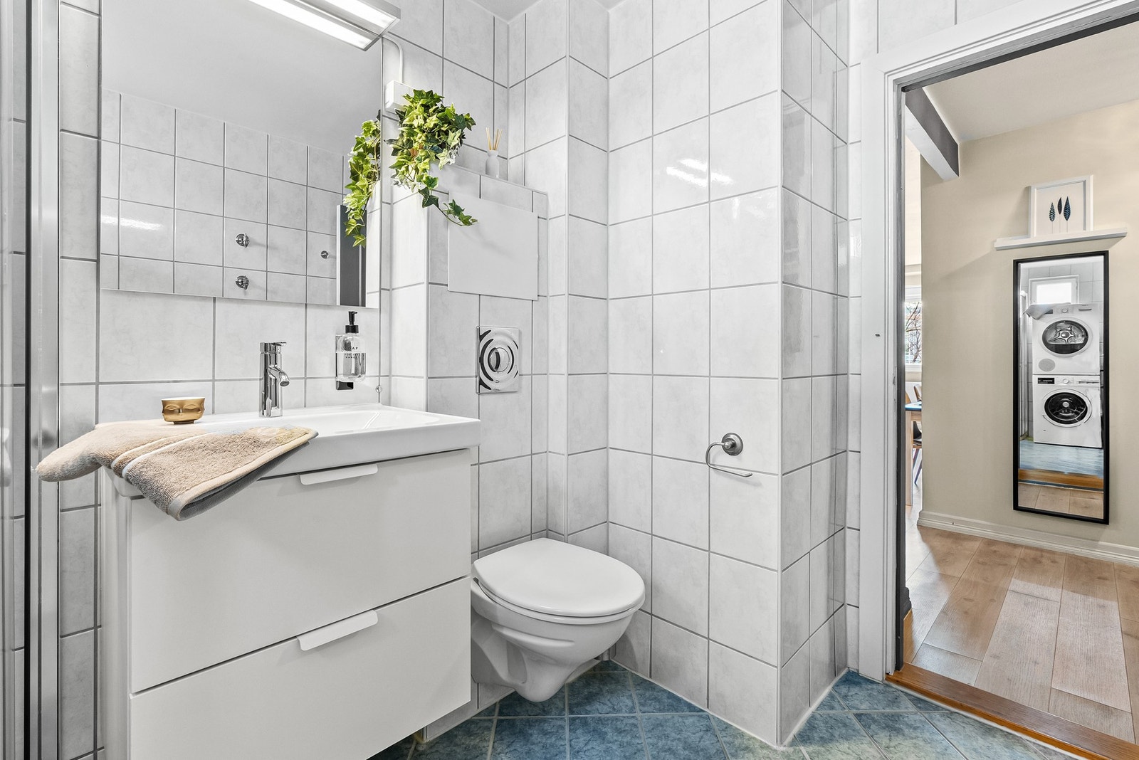 Hvitt servantskap med hvit heldekkende servant, krom blandebatter og speil på vegg. Vegghengt wc og praktisk pyntekant på toppen. Galleribilde