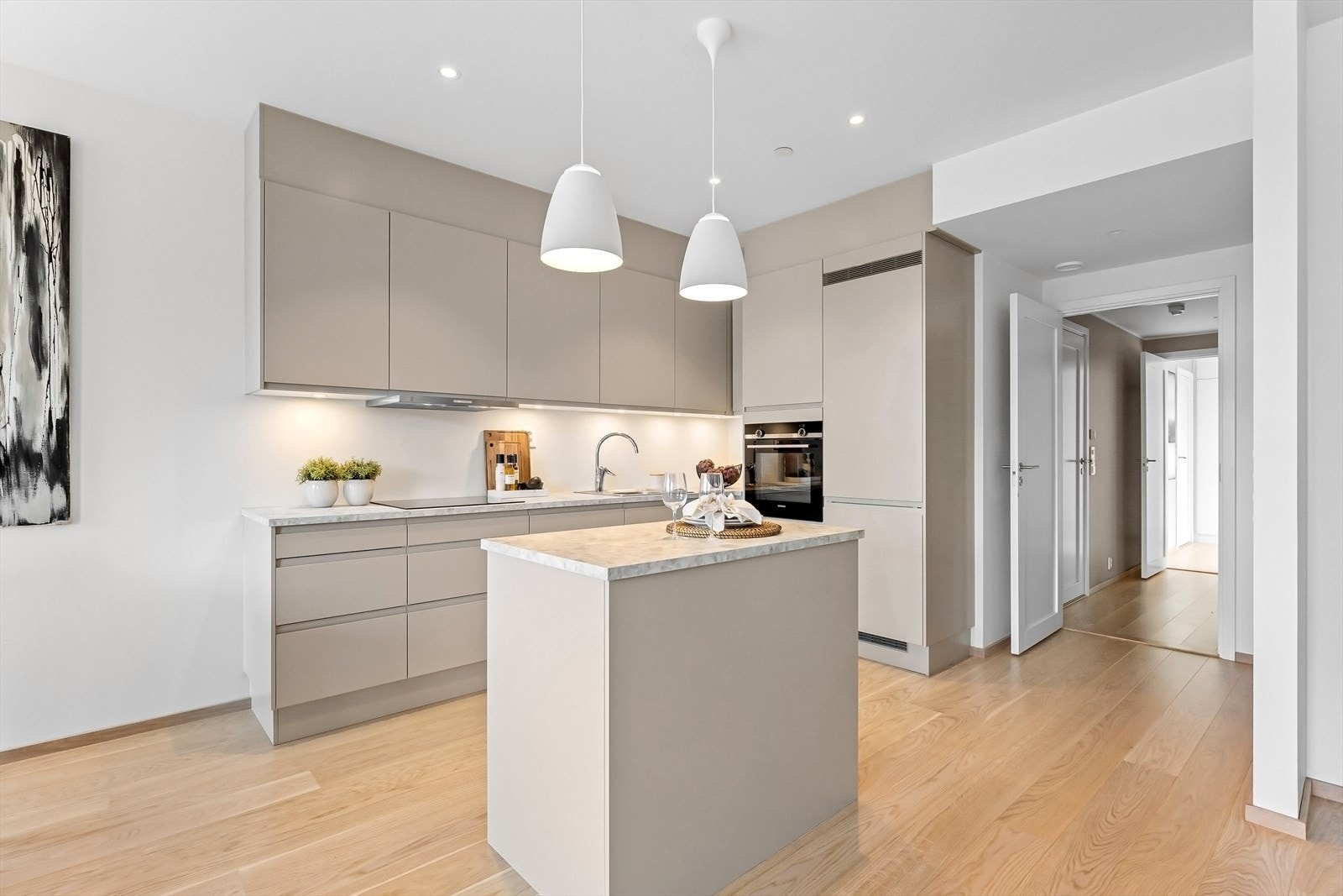 Kjøkkenet har innredning med lysemalte, glatte fronter. Laminat benkeplate som passer godt med leilighetens fargepalett. Her er integrerte hvitevarer fra Siemnes; koketopp, stekovn, oppvaskmaskin og kjøle-/fryseskap. Galleribilde