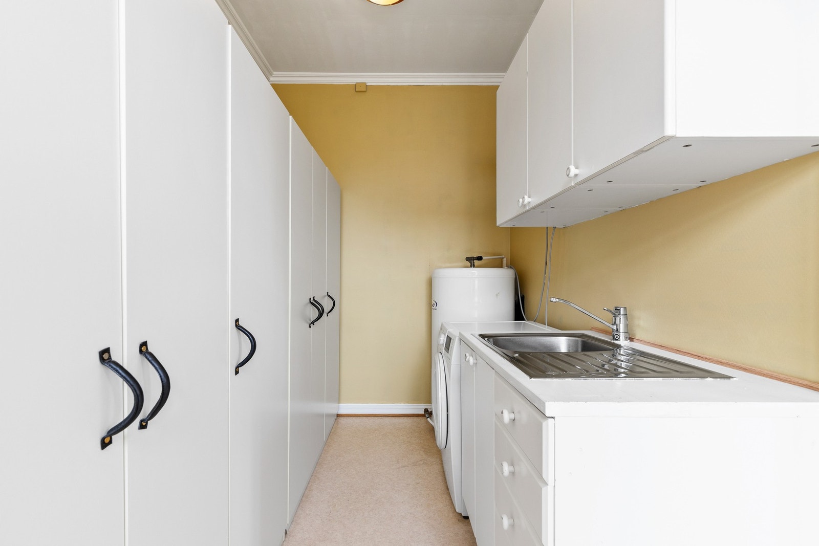 Separat vaskerom med opplegg for vaskemaskin og gulvstående skapinnredning med nedfelt vask Galleribilde