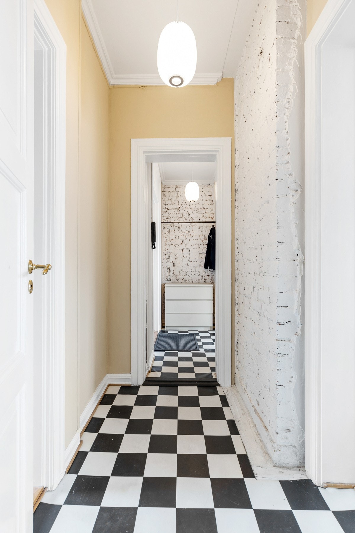 Stilig og lys entré/gang med sjakkmønstret belegg på gulv og innslag av malte teglsteinsvegger Galleribilde