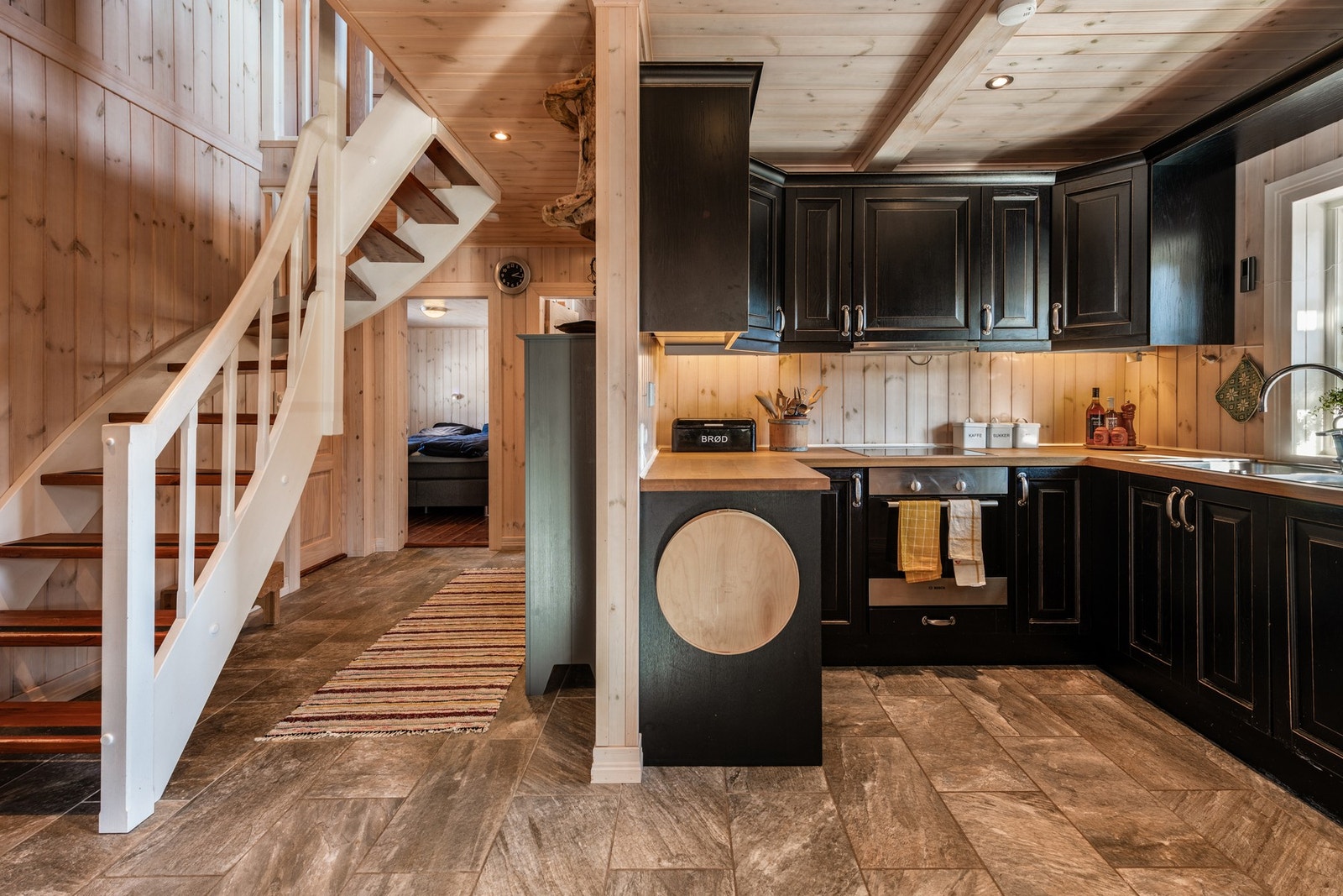 Fra stue og kjøkken går trappen opp til loftsetasjen, og gangen fører videre til soverom og bad Galleribilde