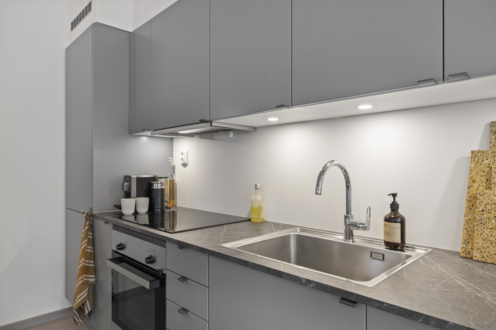 Lekkert kjøkken med innredning i grå slette skapfronter og integrerte hvitevarer Galleribilde