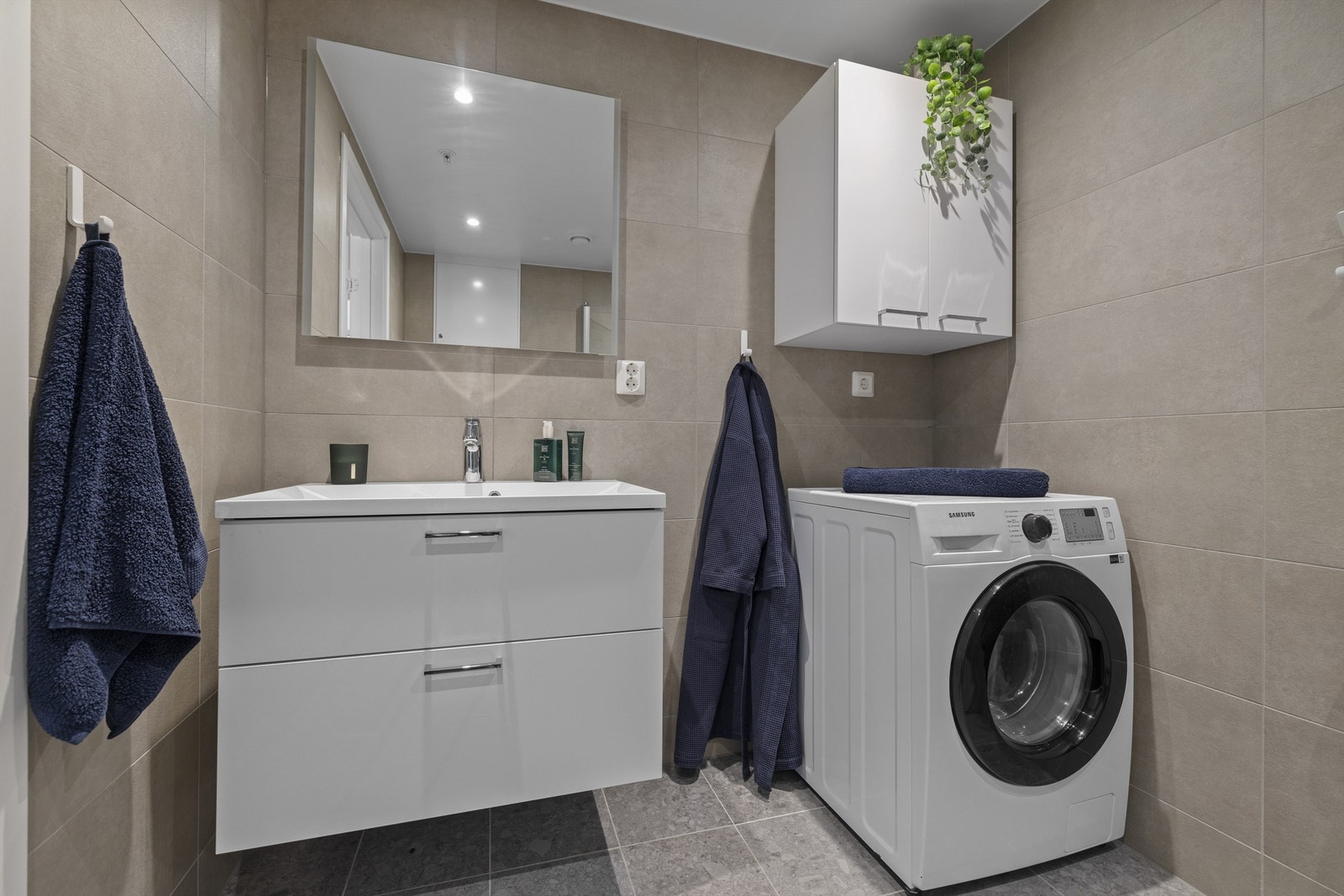 Badet utstyrt med bred servant med dobbel skuffeinnredning, vegghengt speil og toalett, dusjhjørne med innfellbare dører i herdet glass samt dusjsett med rainshower Galleribilde