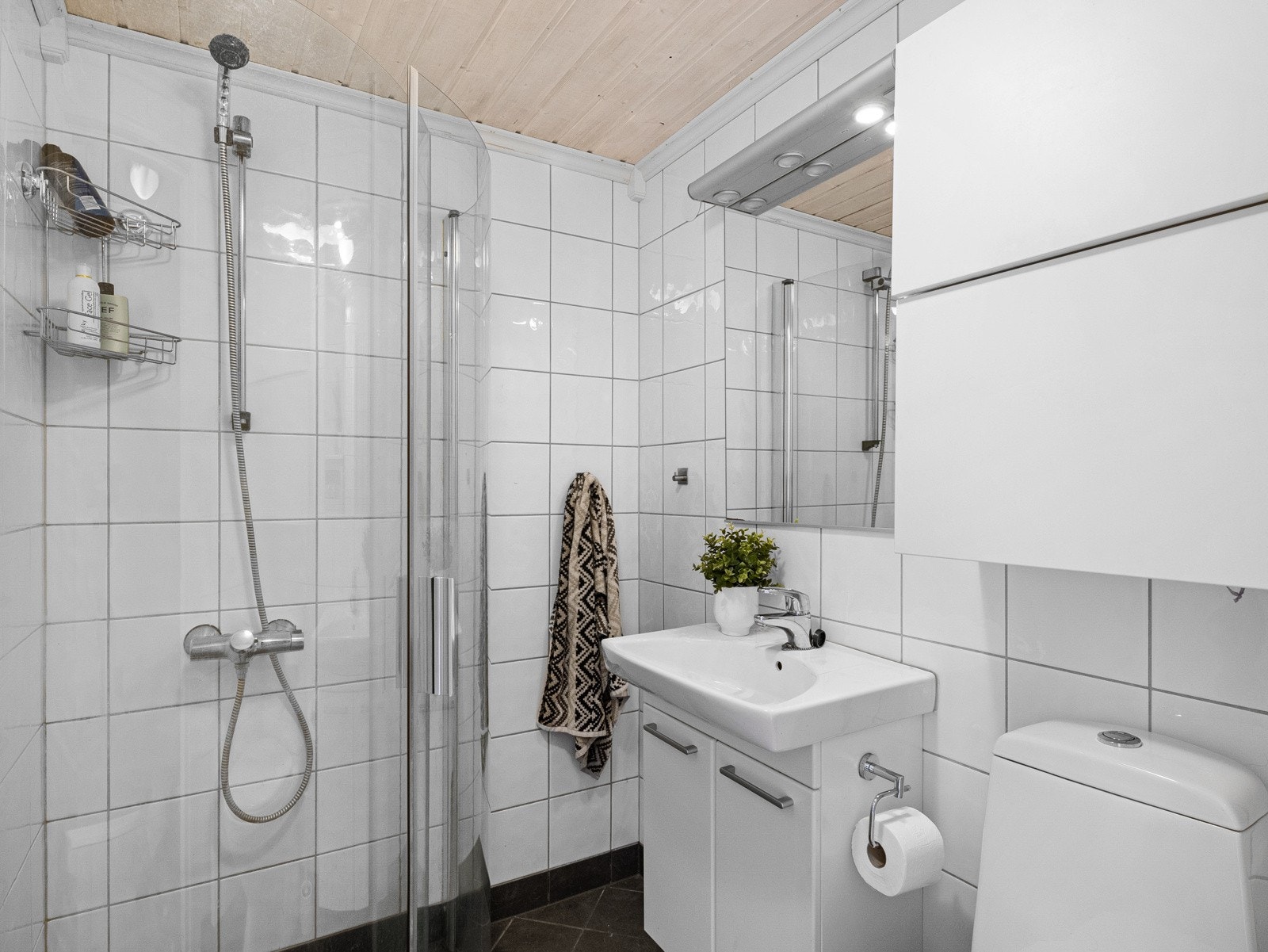 Badet er på ca. 2,7 utført med fliser på gulv og vegger og inneholder benkeskap med servant, gulvmontert toalett og dusjdører i glass. Galleribilde