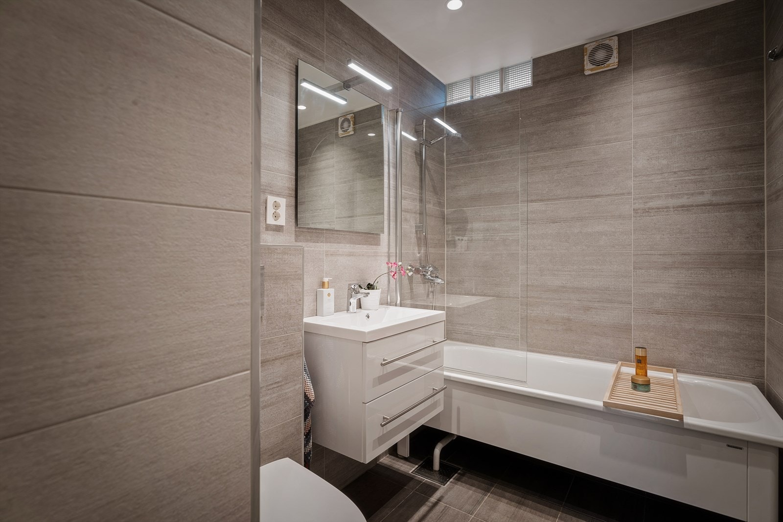 Romslig flislagt bad fra 2017. Rommet er innredet med badekar med dusjhjørne, servantskap med skuffeseksjon, speil og vegghengt toalett. Galleribilde