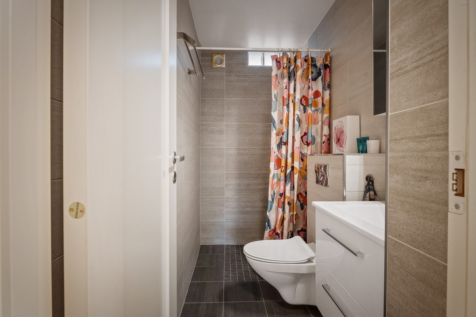 Pent flislagt bad fra 2017. Rommet er innredet med dusjhjørne, servantskap med skuffeseksjon, speilskap og vegghengt toalett. Galleribilde