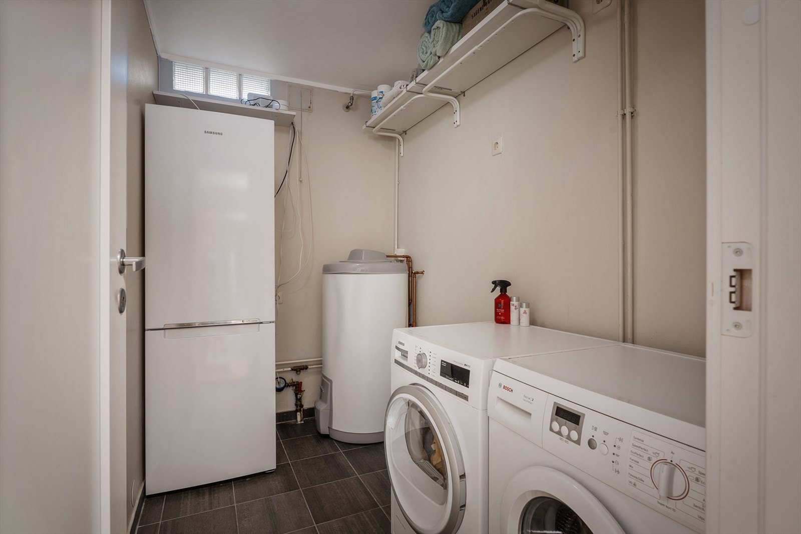 Praktisk tekniskrom/vaskerom med flislagt gulv. Rommet er innredet med varmtvannsbereder på ca. 200 liter, vannskap, opplegg for vaskemaskin og tørketrommel. Galleribilde