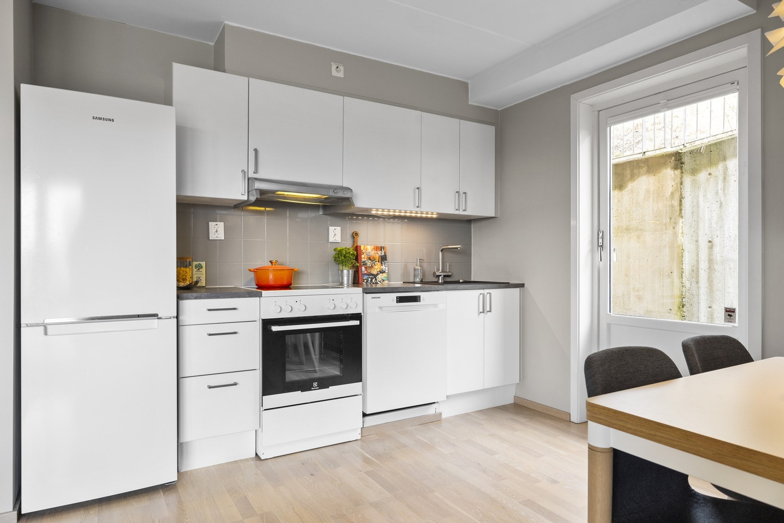 Kjøkkeninnredning fra Sigdal med hvite fronter og håndtak. Benkeplate av laminert spon. Nisje til oppvaskmaskin, komfyr og kjøl/frys. Galleribilde