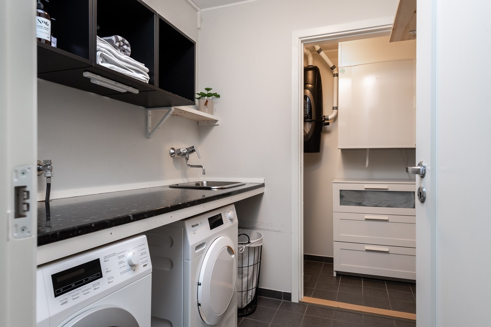 Praktisk vaskerom med flislagt gulv og opplegg for vaskemaskin, perfekt for organisering av klesvasken. Galleribilde