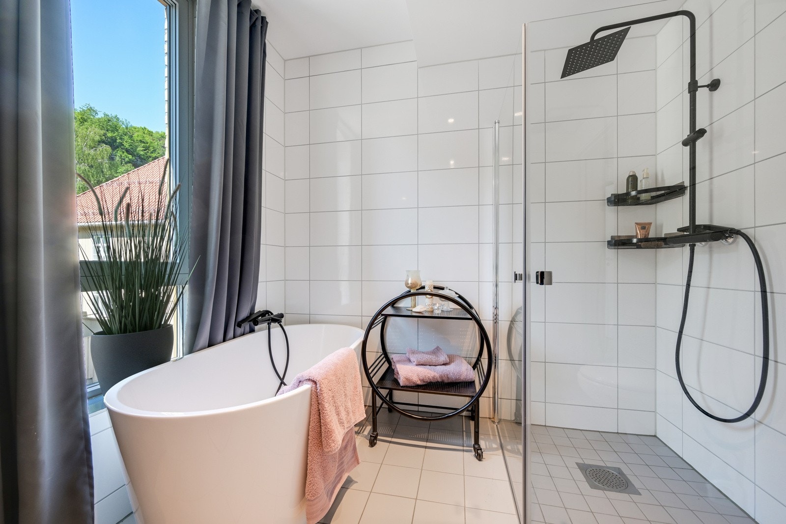 Badet er innredet med slette fronter, heldekkende servant, vegghengt toalett, dusjhjørne med glassdører og frittstående badekar Galleribilde