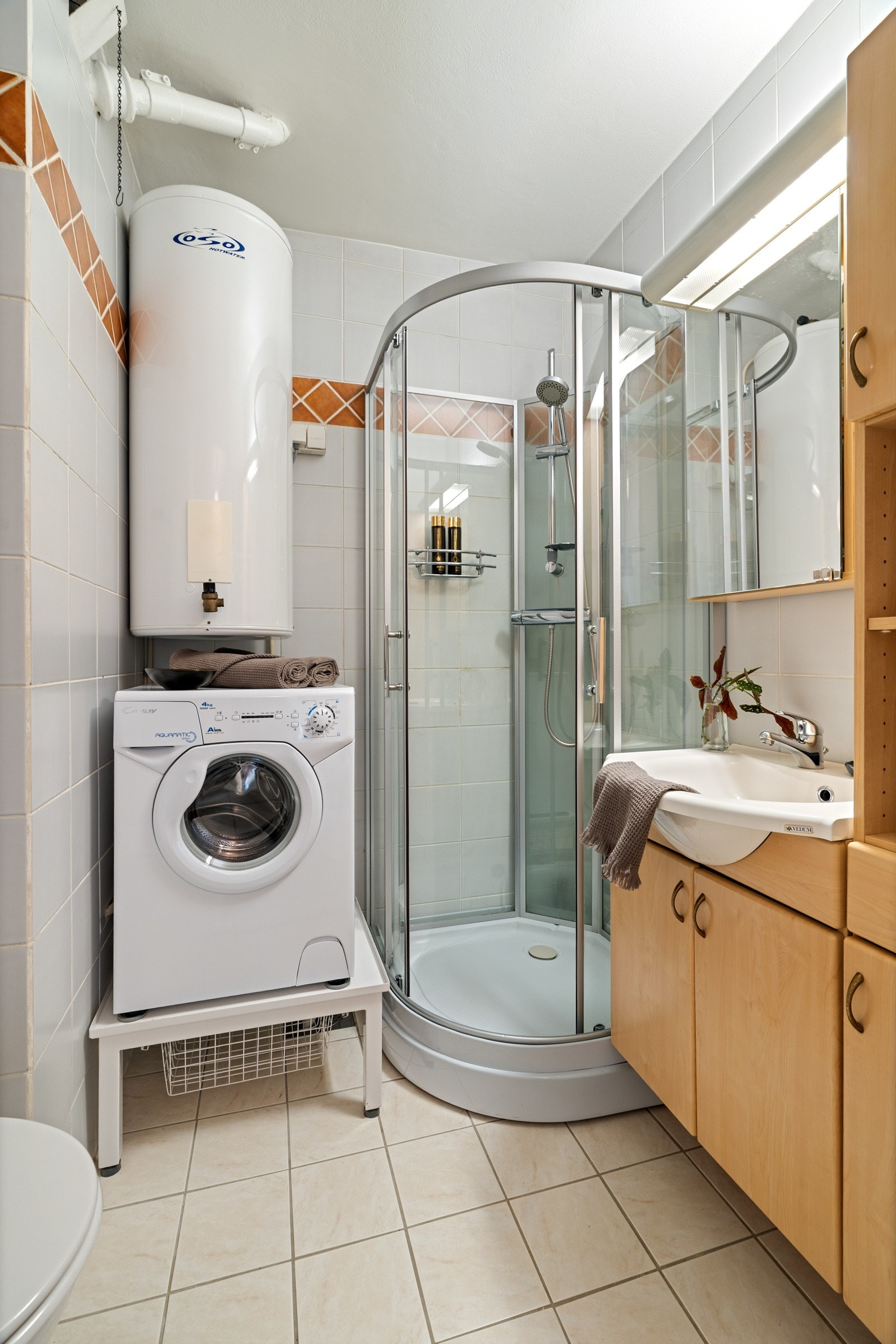 Badet er flislagt på både vegger og gulv. Her er det innredet med servant og servantskap med mye oppbevaringsmuligheter. Det er også innredet med dusjkabinett og toalett, samt plass til vaskemaskin. Galleribilde