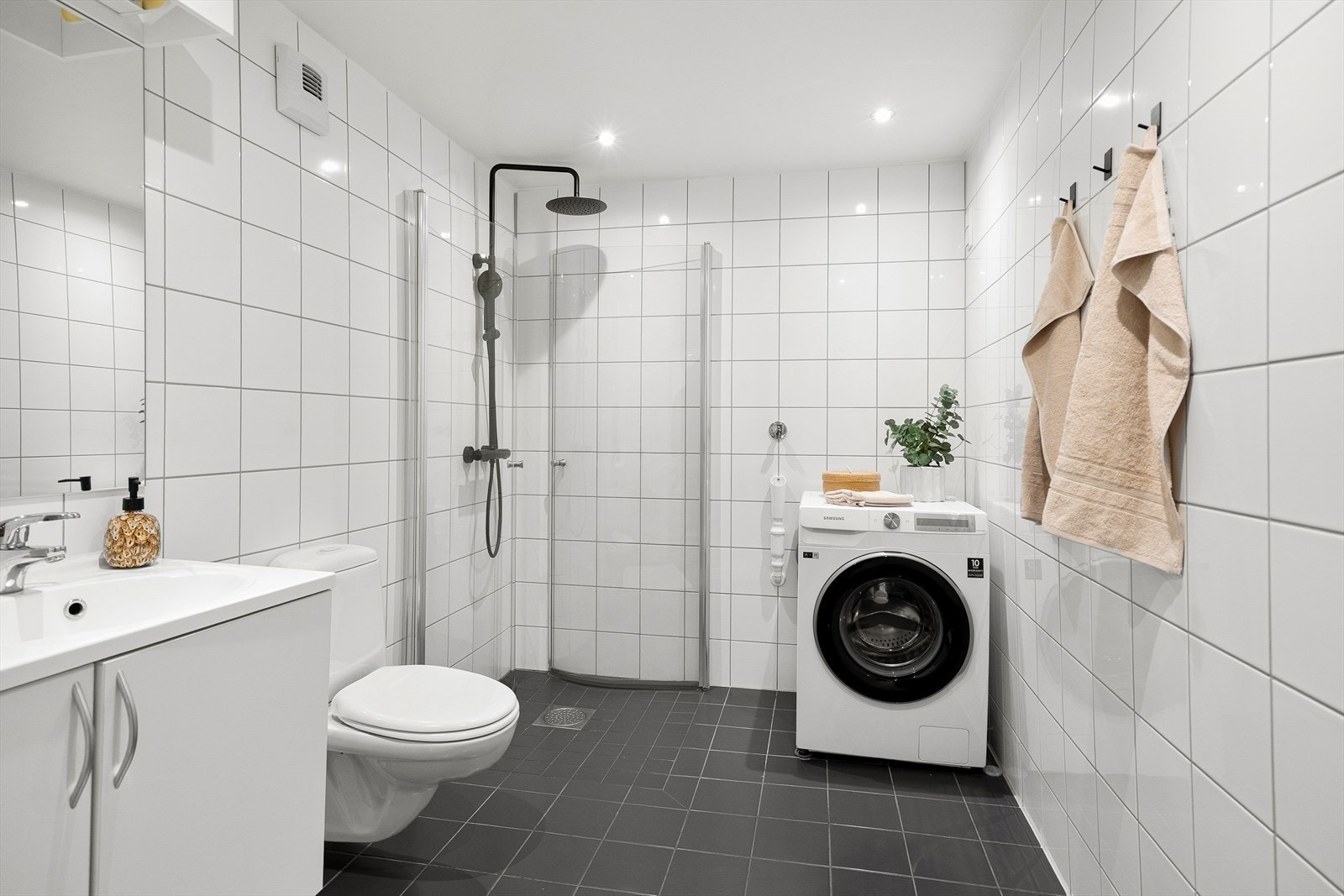 Badet er innredet med innfellbare dusjdører, opplegg for vaskemaskin, servantskap og veggmontert wc Galleribilde