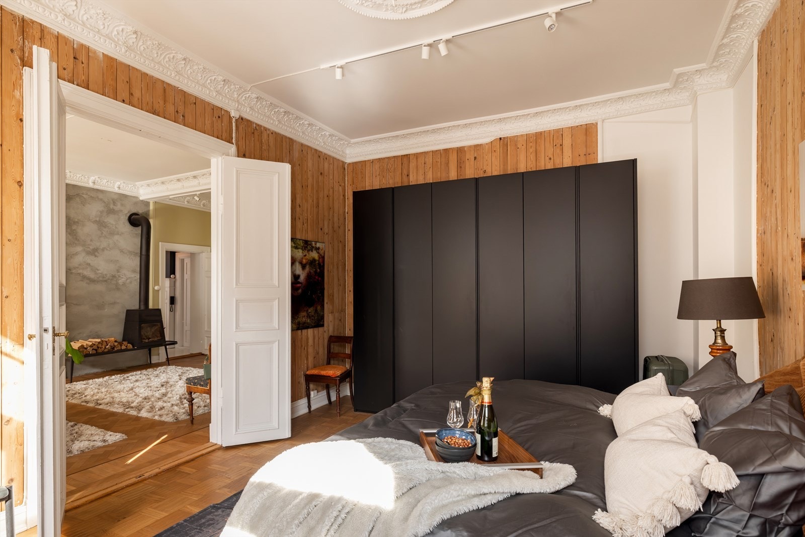 Et romslig og stilfullt soverom med parkett i rutemønster og tofløyede profilerte dører fra stuen. Rommet har en eksklusiv garderobeinnredning fra Lema, installert i 2016, samt takskinner med spotbelysning og elegante designpendler. Galleribilde