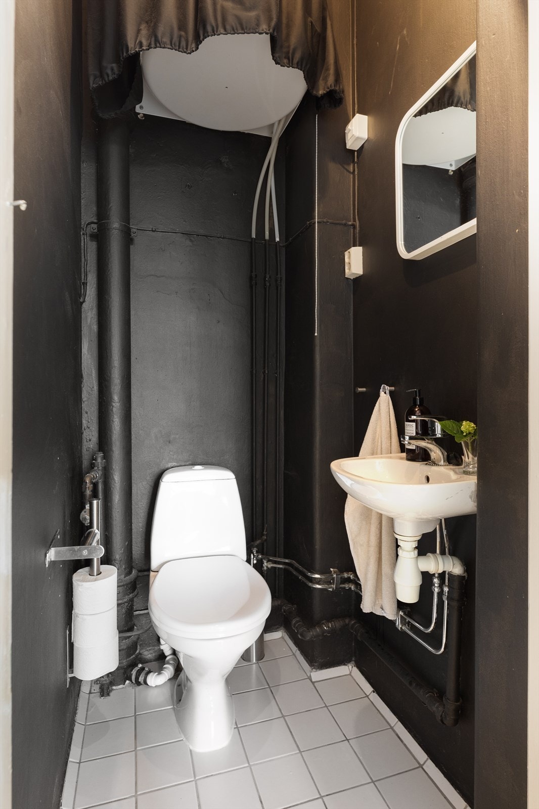 Separert toalettrom i en mørk utførelse, bestående av gulvstående toalett, speil og servant. Galleribilde