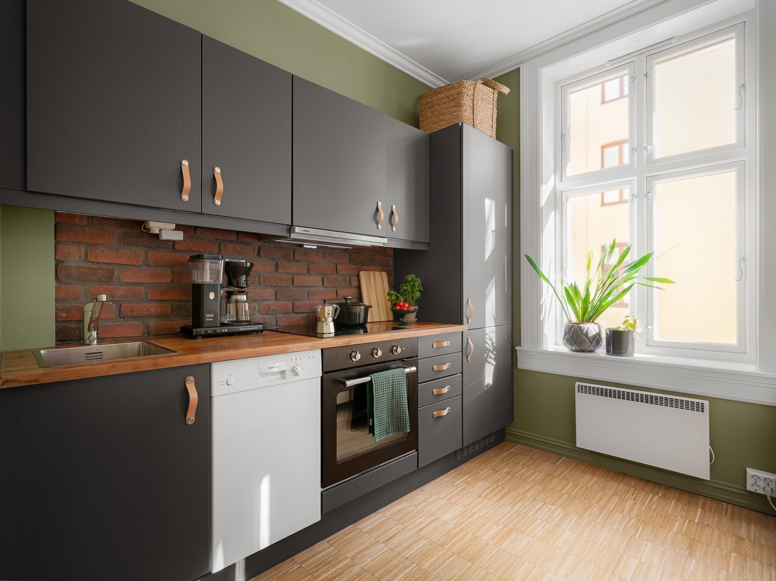 Kjøkkeninnredningen fra HTH har gråmalte fronter, laminat benkeplate og nedfelt rustfri oppvaskkum, samt ettgreps kjøkkenbatteri. Teglstein mellom over- og underskap skaper et tøft særpreg. Galleribilde