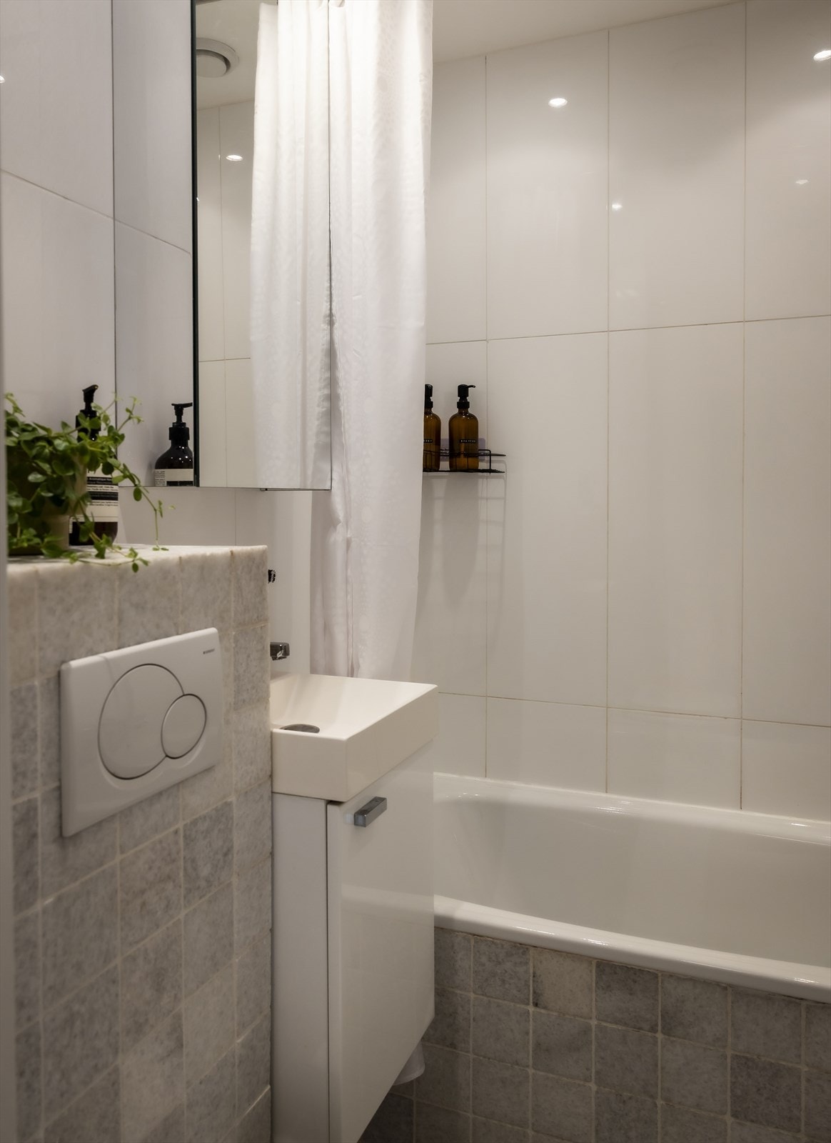 Badet er innredet med servant med underskap, overskap med speildører, vegghengt toalett og innfliset badekar med dusjforheng og armatur på vegg. Galleribilde