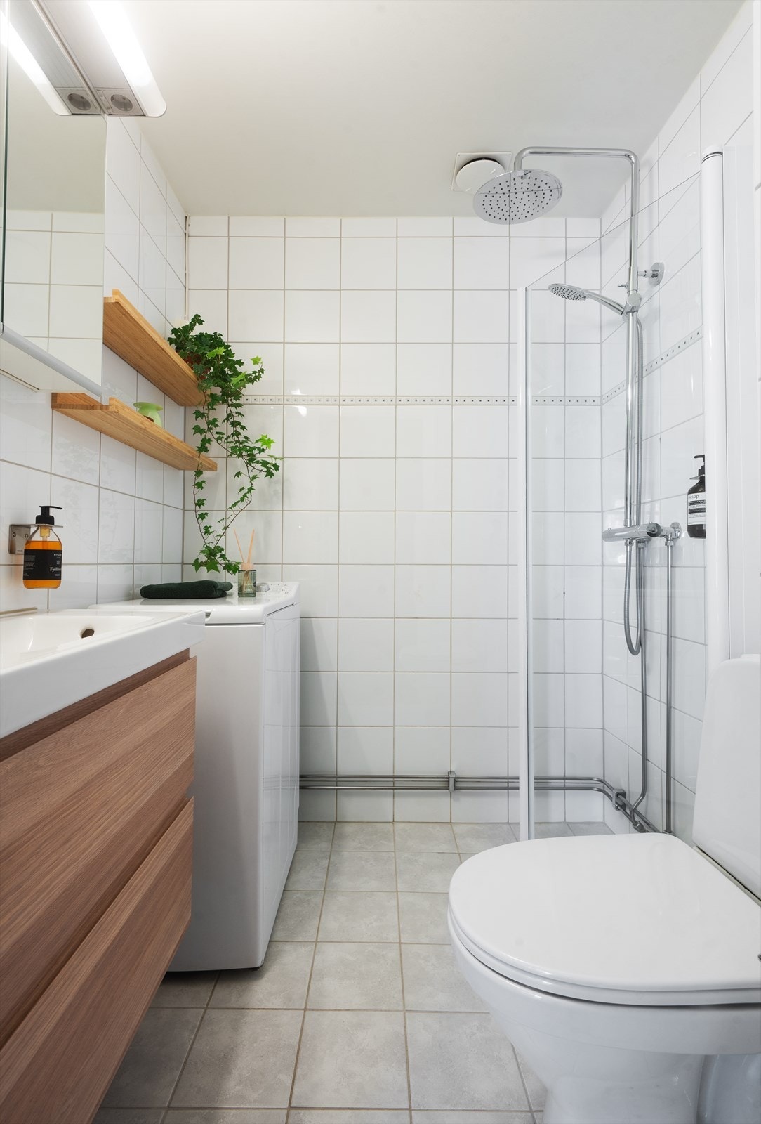 Innredning med gulvstående toalett, servant med ettgreps blandebatteri, dusjarmatur, plass og opplegg for vaskemaskin og speilskap med belysning. Galleribilde