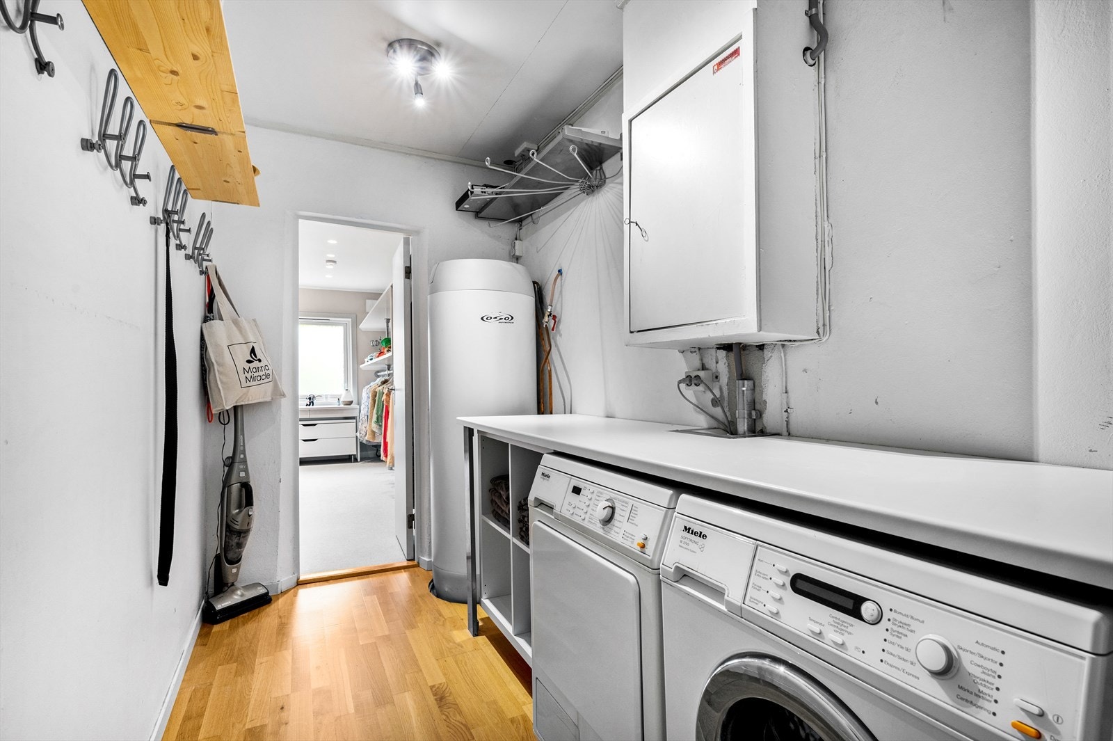 Vaskerom med praktisk arbeidsbenk, utstyrt med opplegg for vaskemaskin og tørketrommel, varmtvannsbereder og sikringsskap. Galleribilde