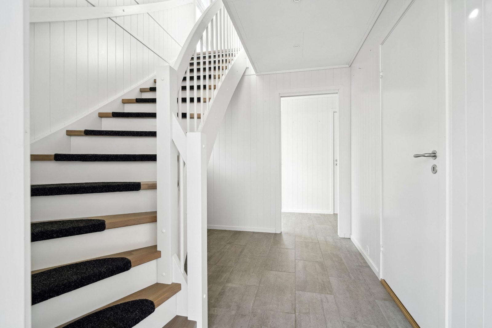 Lyst og moderne gangområde med trapp til andre etasje og flislagt gulv. Galleribilde