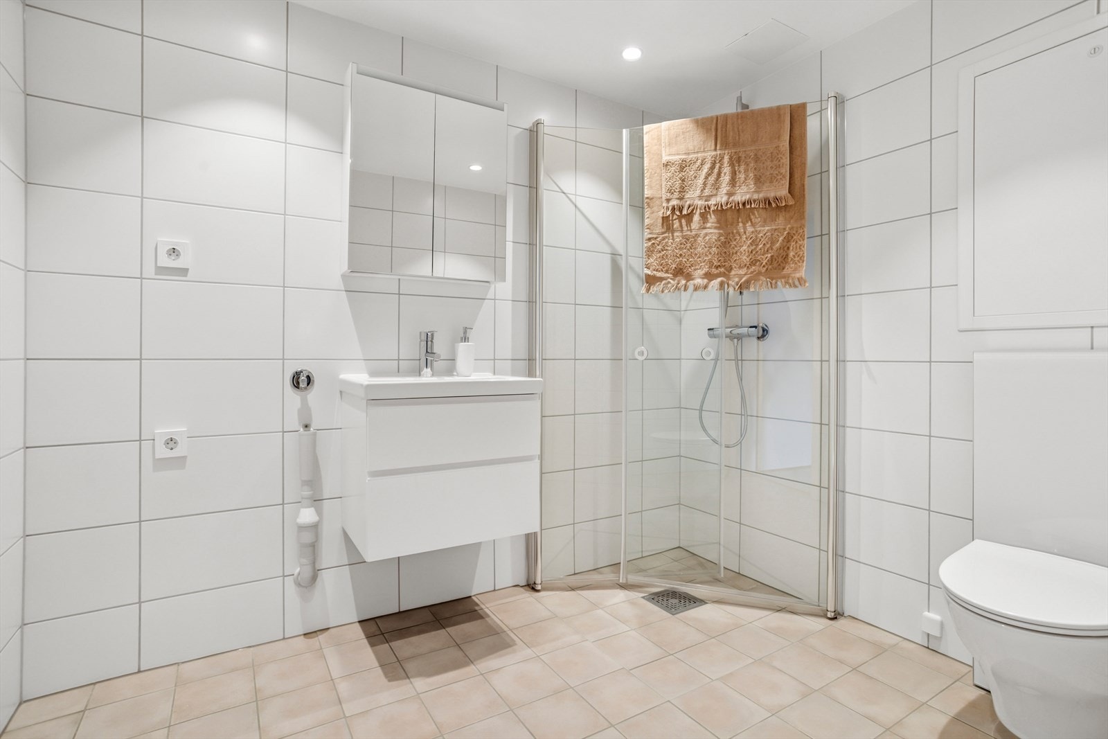 Badet er utstyrt med servant med skuffer, dusjhjørne, vegghengt toalett, opplegg for vaskemaskin og gulvvarme. Galleribilde