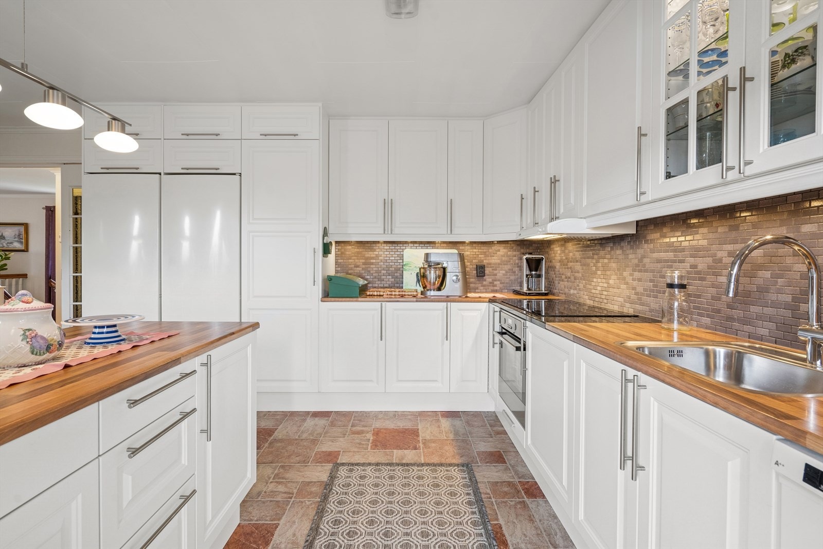 Det er integrert komfyr og platetopp, samt frittstående oppvaskmaskin, kjøleskap og fryseskap. Over benken er det fliser på veggen, og kjøkkenventilatoren har avtrekk ut. Galleribilde