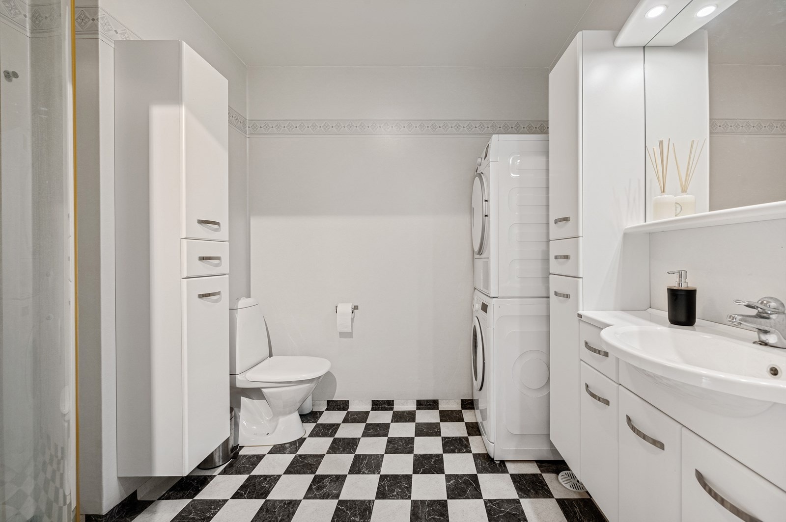 Lyst bad med dusjhjørne, toalett og praktisk baderomsinnredning. Opplegg for vaskemaskin og tørketrommel. Galleribilde