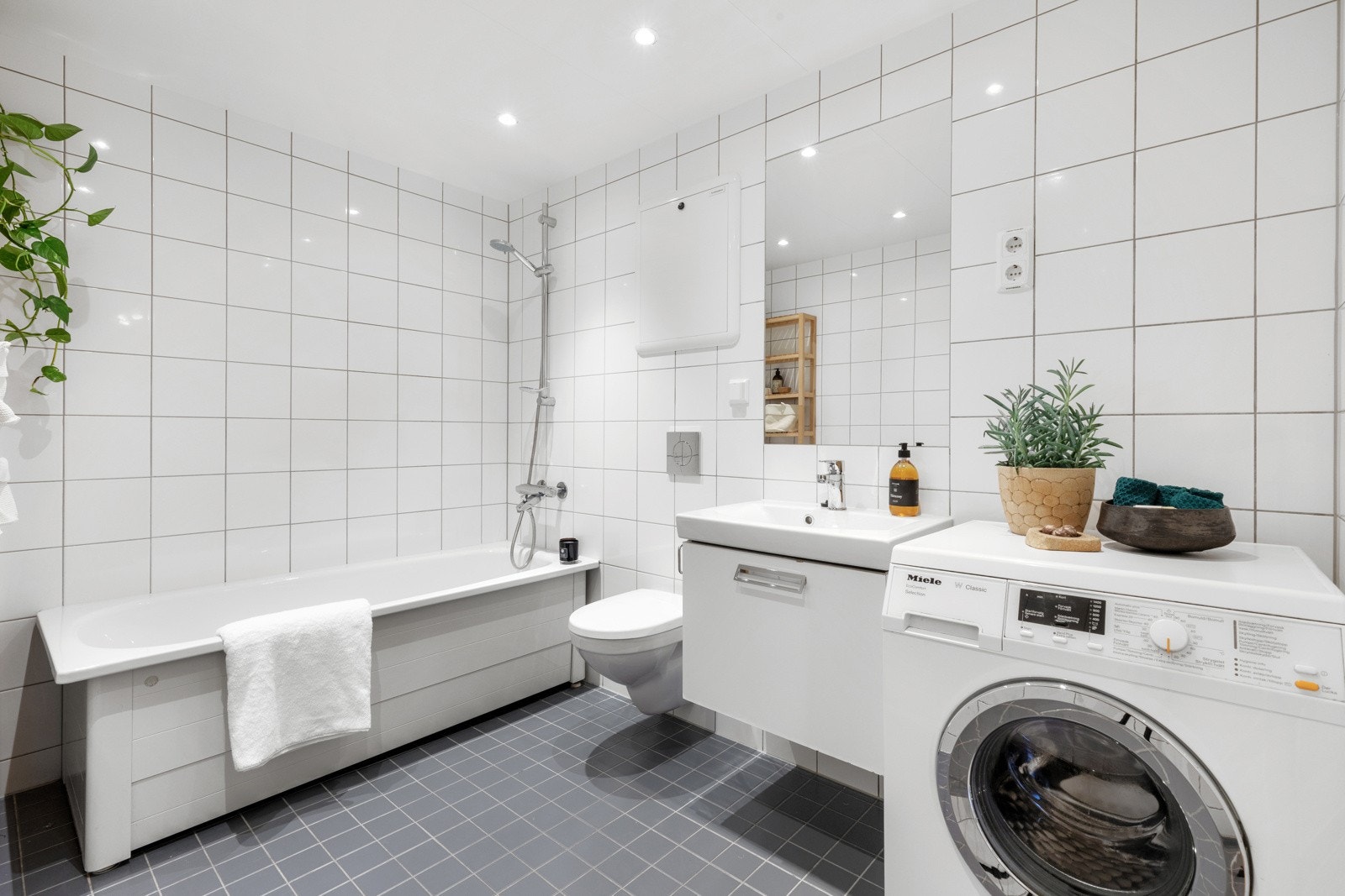 Baderommet inneholder servant med underskap, speil med overbelysning, gulvstående høyskap, toalett og badekar. Galleribilde