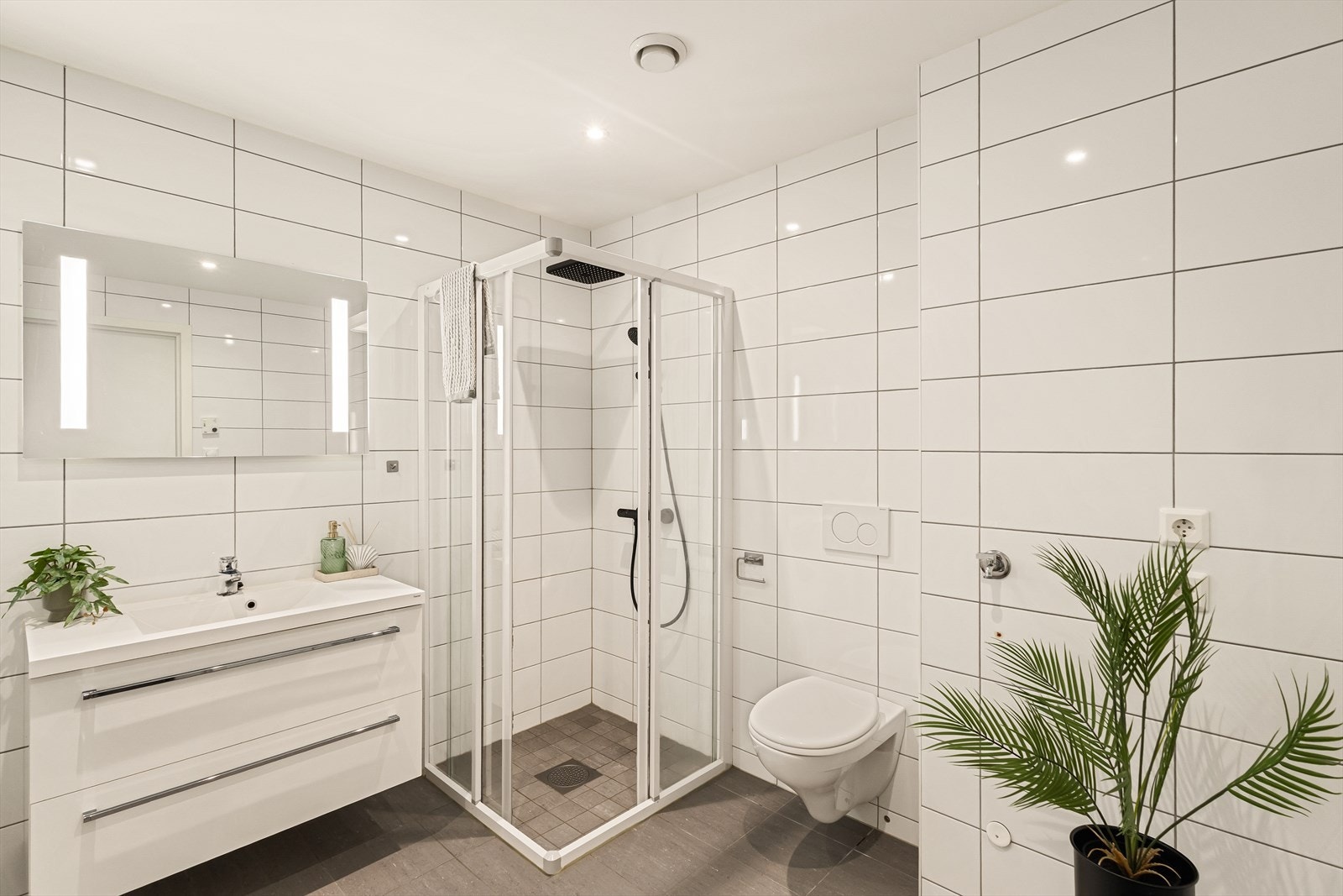 Badet er av god størrelse og har dusjhjørne, vegghengt toalett og praktisk innredning med servant Galleribilde