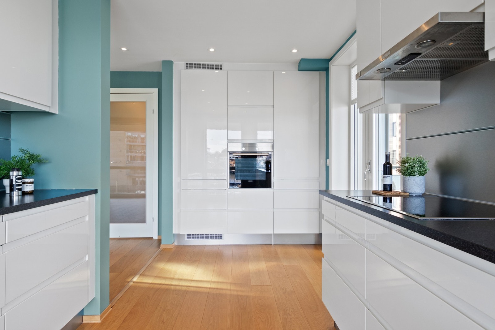 Innredningen har takhøye skap, glatte, hvite høyglansfronter med gripekant, mørk benkeplate i laminat med planlimt vaskekum og plater i børstet aluminium som backsplash. Galleribilde