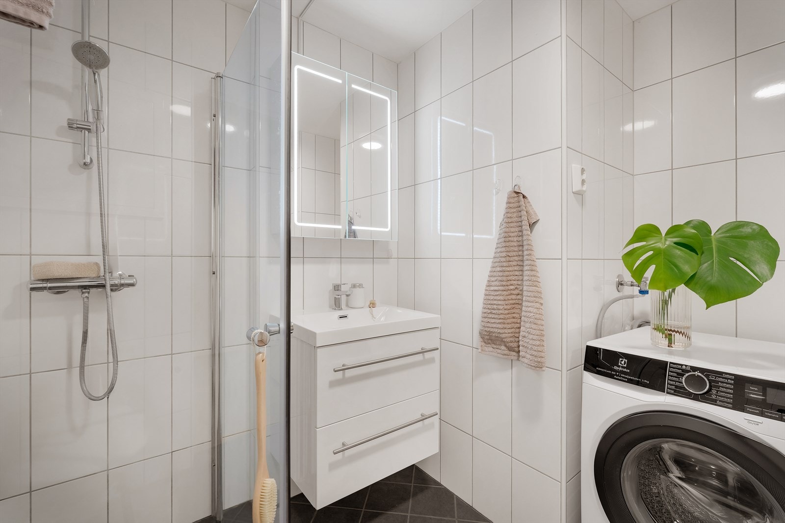 - Badet er innredet med vegghengt toalett, benkeskap med servant, opplegg for vaskemaskin og dusjdører i glass - Galleribilde