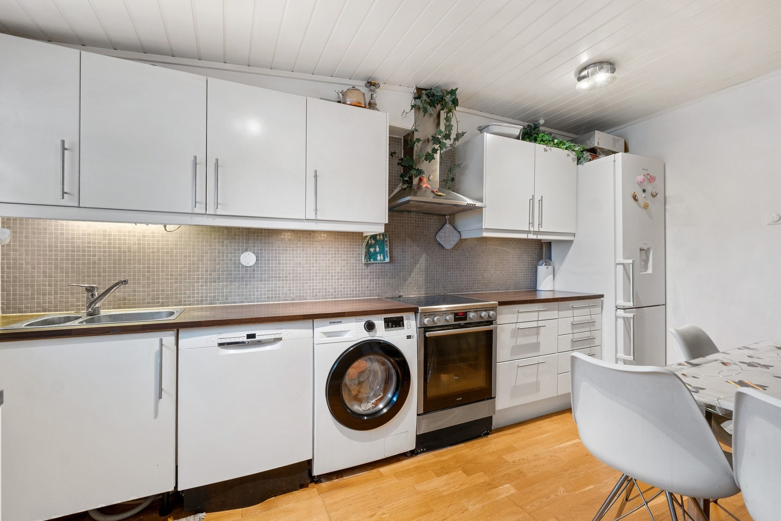 Stilren, hvit innredning med benkeplate i stilen av mørkt tre. Opplegg for hvitevarer. Galleribilde