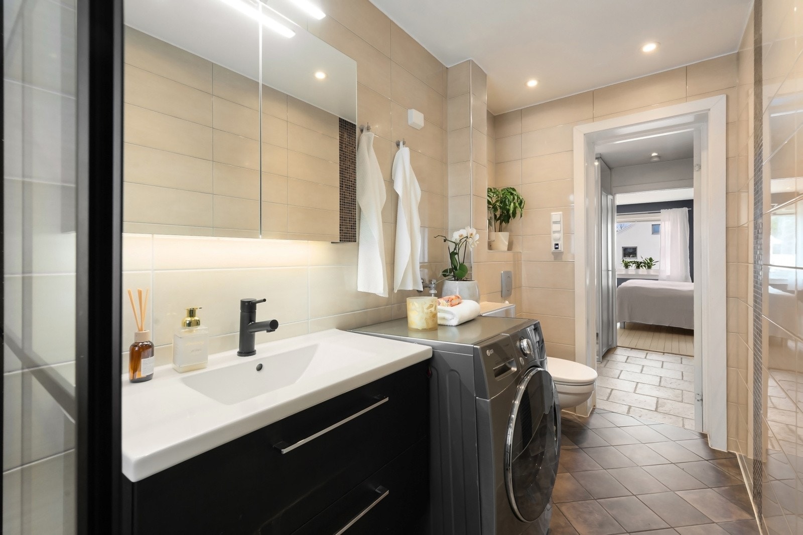 Badet har vegghengt toalett, speilskap med integrert belysning og porselenservant med mørke servantskap og ettgreps armatur. Galleribilde