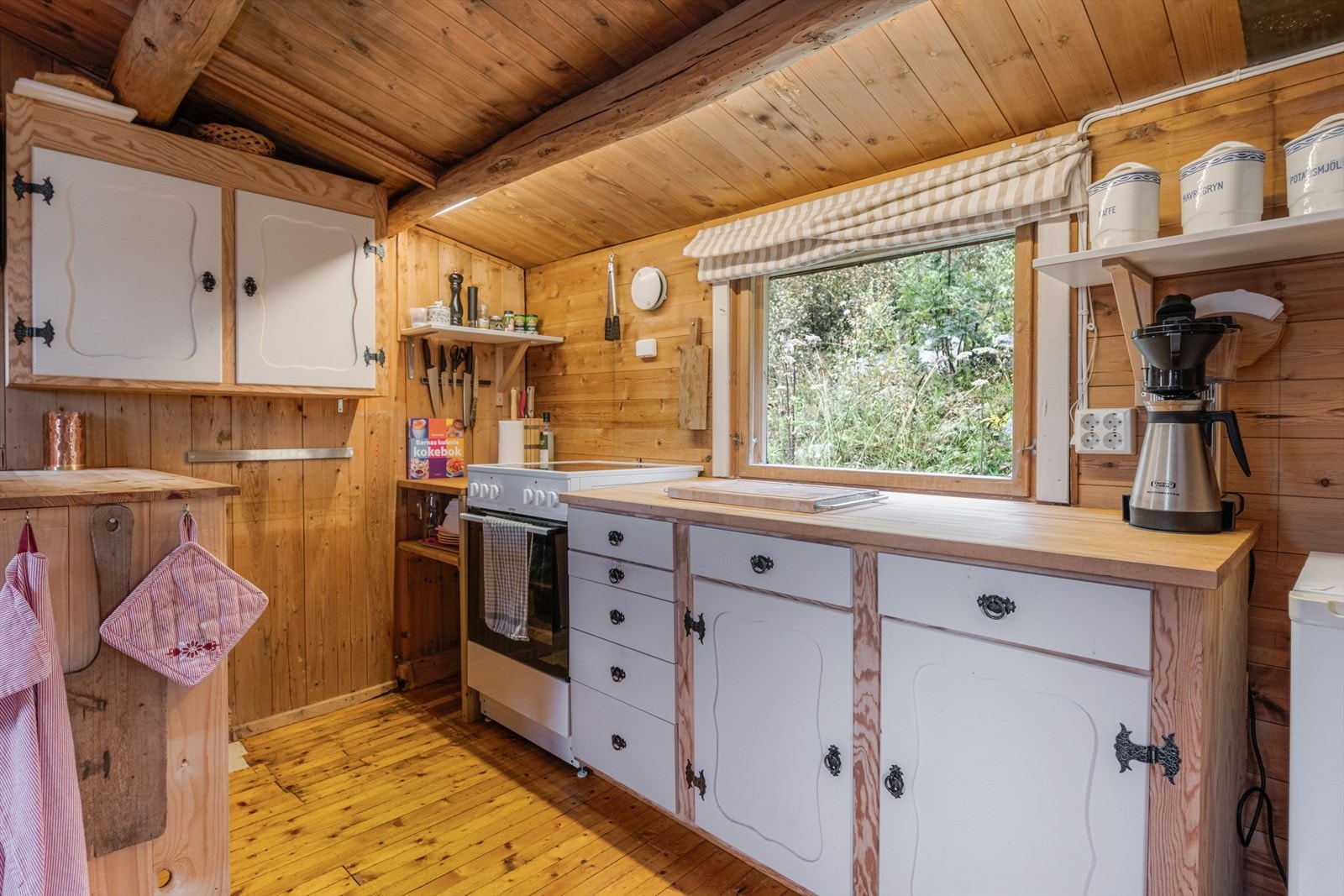 Kjøkkenet har eldre innredning med profilerte fronter som er hvitmalt. Benkeplater av laminat og plass for frittstående komfyr og kjøleskap, og på motsatt vegg er det nedfelt oppvaskkum. Galleribilde