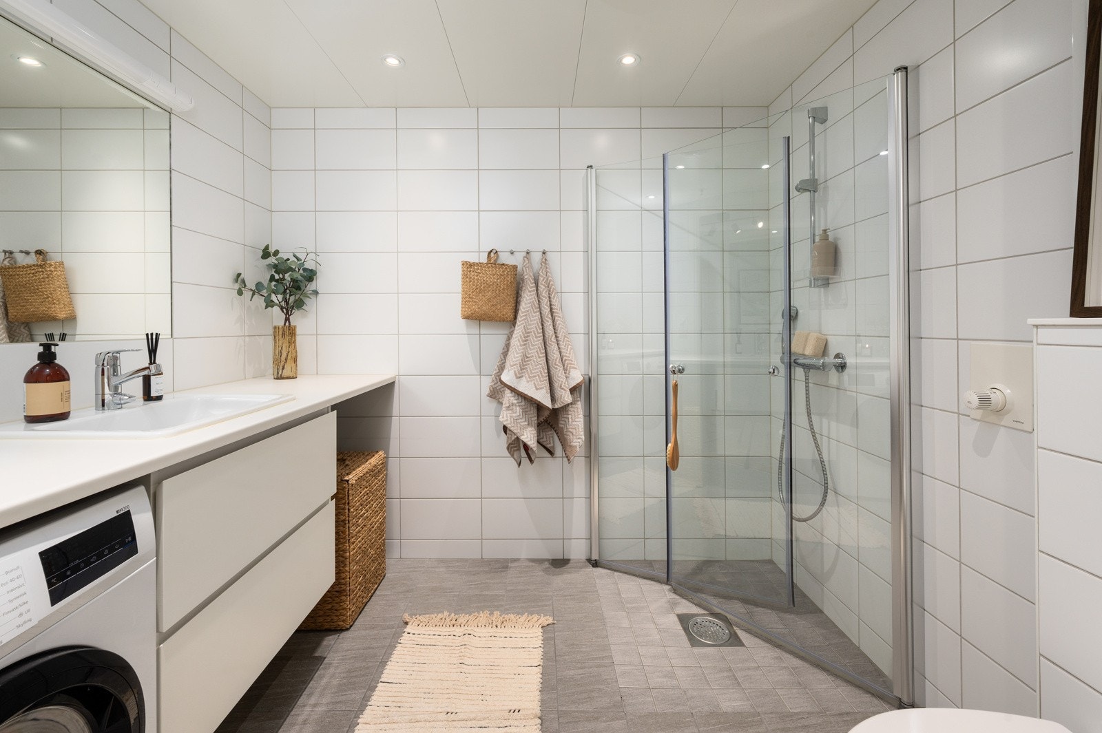 Leilighetens baderom fremstår som moderne og funksjonelt, med flislagte vegger og himling med lyse panelplater Galleribilde