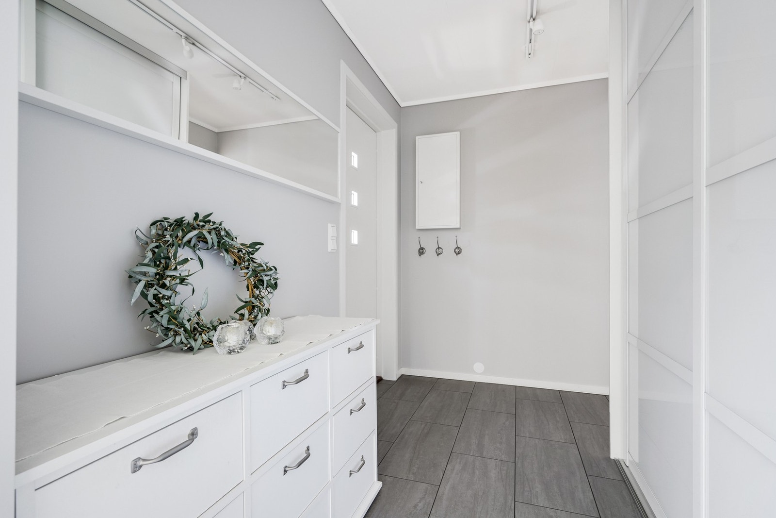 Innbydende og delikat inngangsparti med Elfa skyvedørsgarderobe som gir en praktisk løsning for oppbevaring av klær og sko. Her har barna knagger i tilpasset høyde. Galleribilde